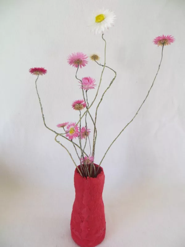 flores secas de color rosa con pequeño jarrón de papel maché